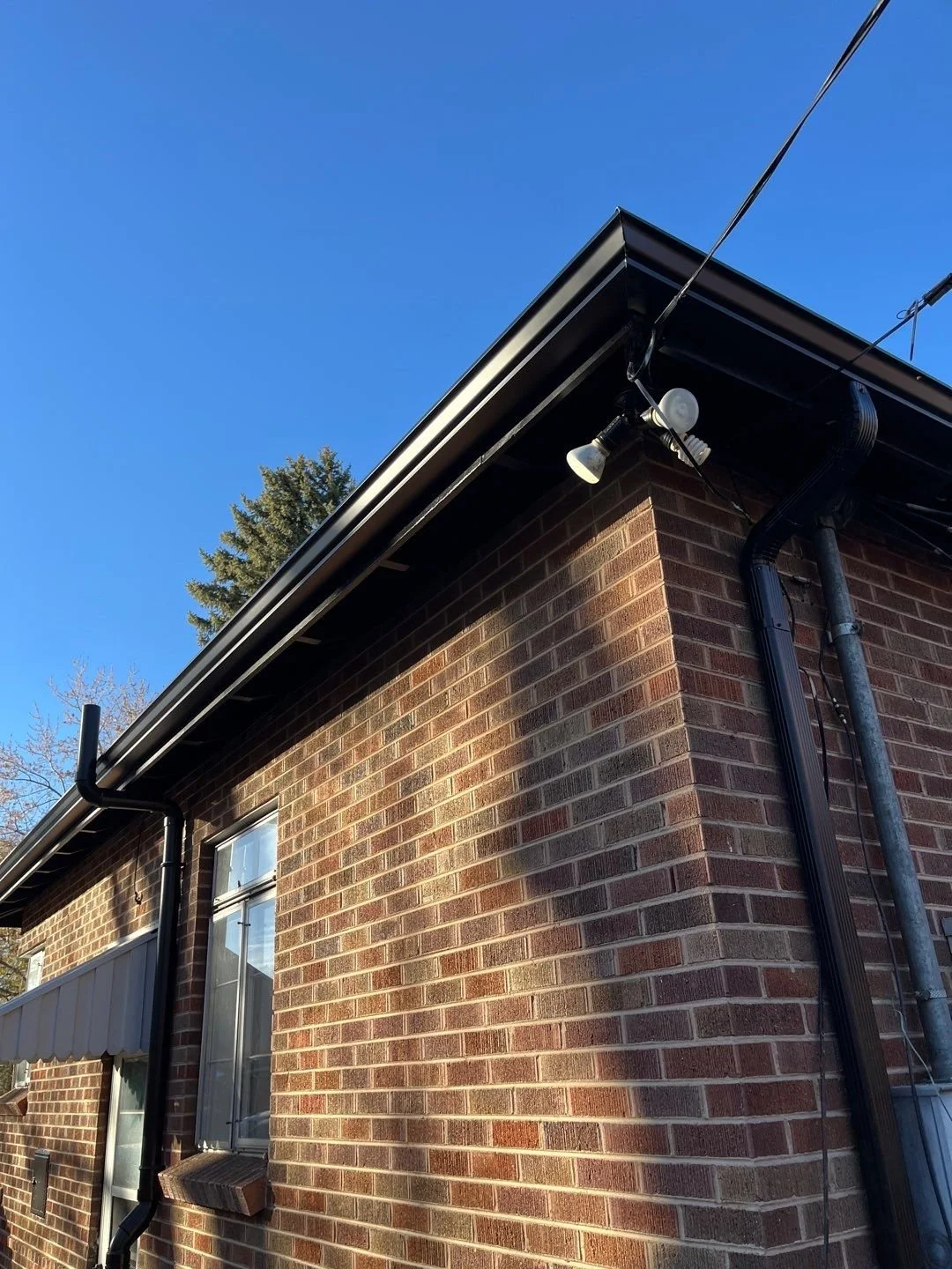 Seamless gutter and downspout system installed along the upper roofline of a brick home.