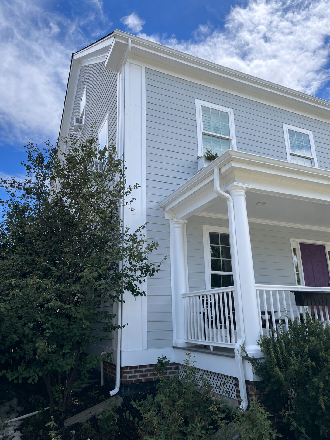 Seamless gutters and downspouts installed on a two-story home with a covered front porch.