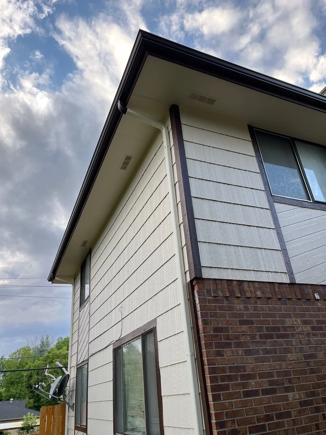 Residential gutter replacement finished along the corner of a brick-and-siding home.