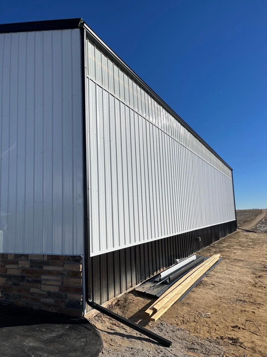 Seamless gutter installation on a metal building roofline with custom drainage placement.