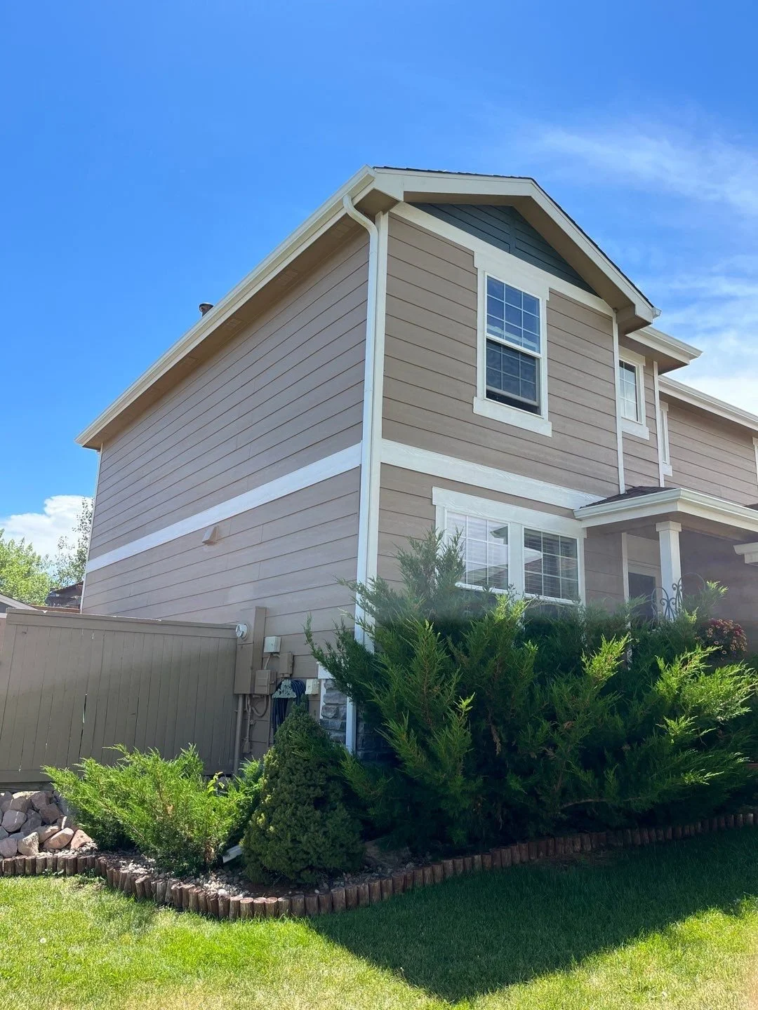White seamless gutters and downspouts installed on a tan two-story home.