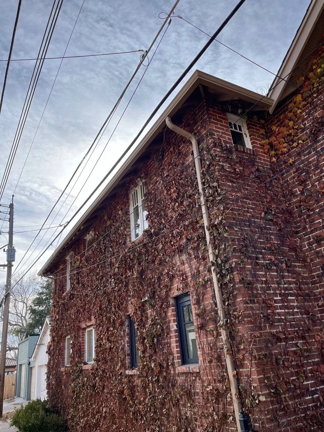 Close-up of a seamless gutter and downspout system installed along a tall brick exterior wall.
