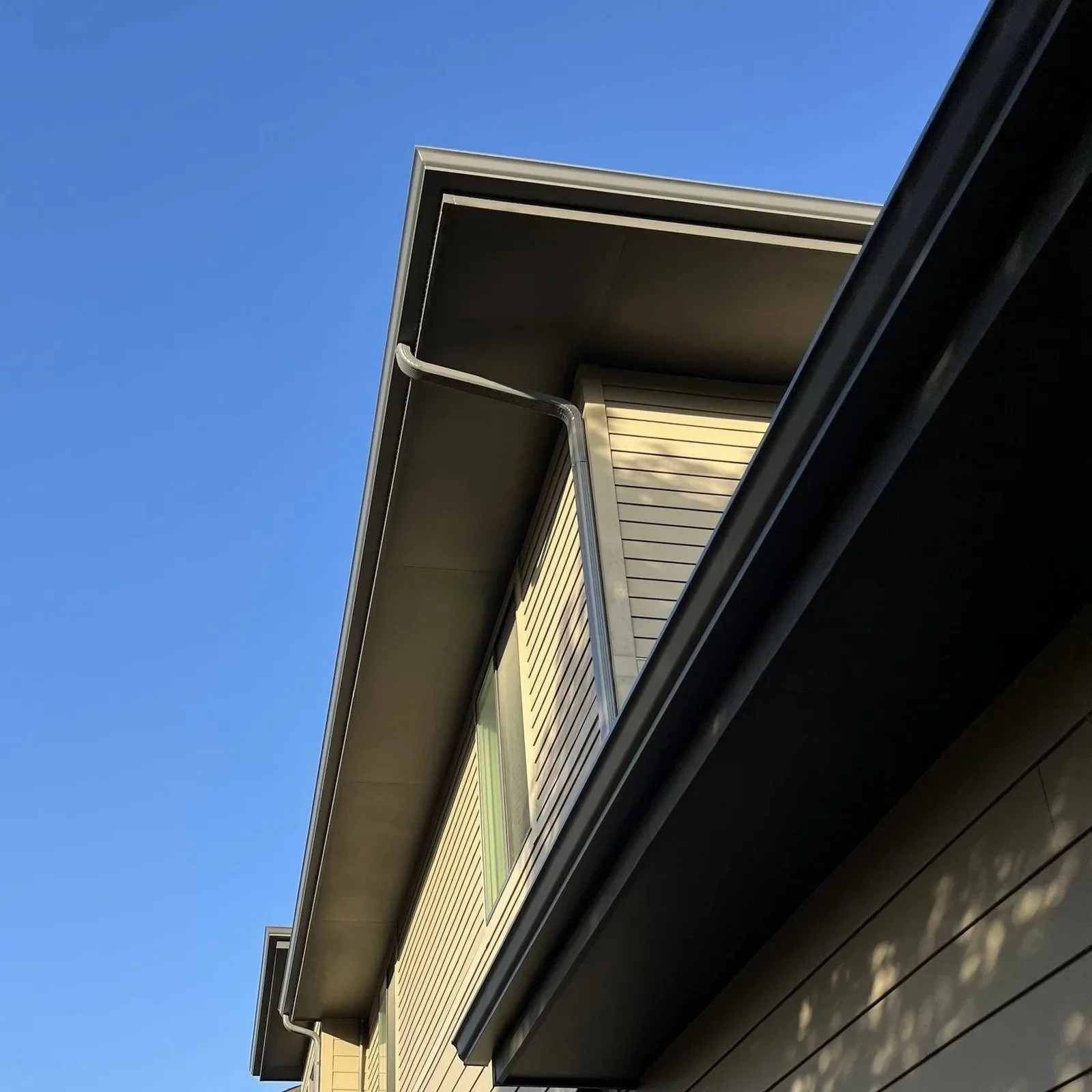 Seamless gutter and offset downspout installed along the upper roofline of a two-story home.