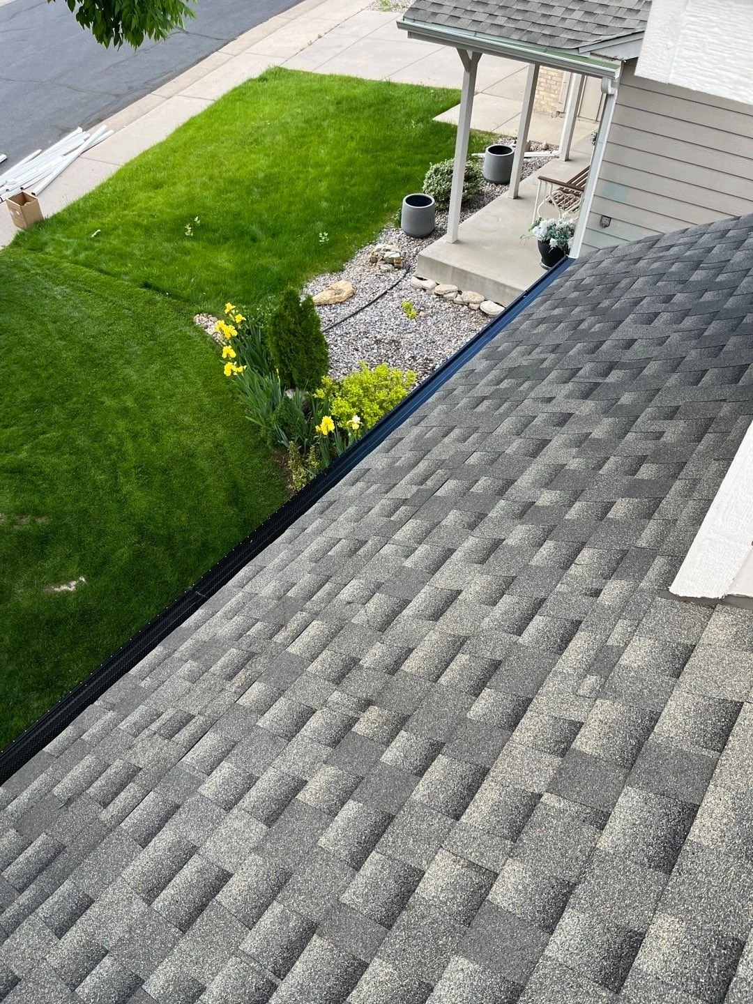 Roof-level view of a seamless gutter and gutter guard installation along a residential shingle roofline.