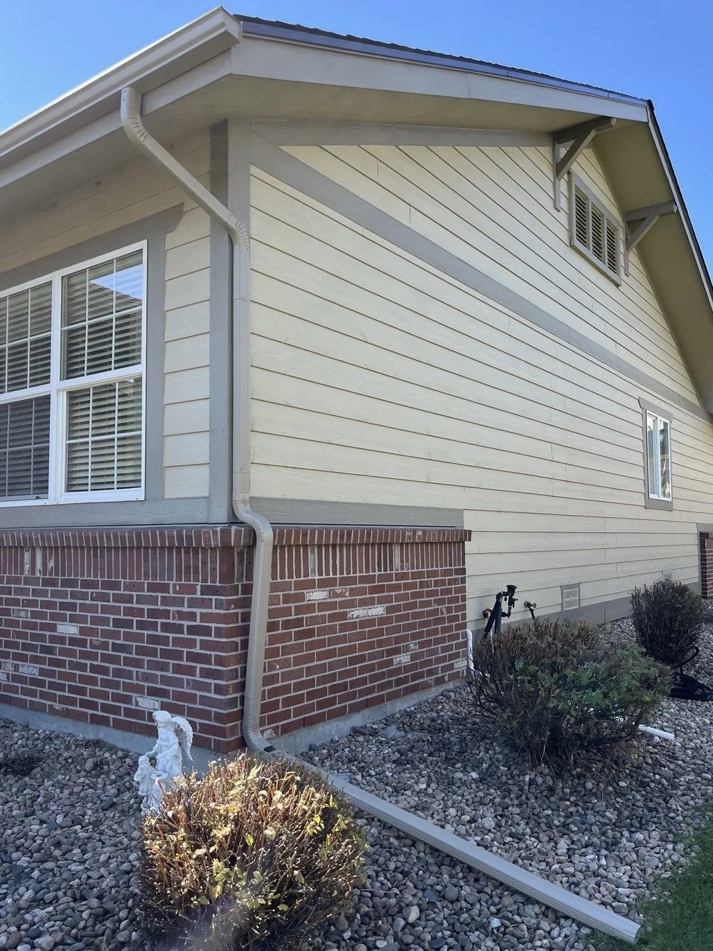 New seamless gutter and downspout system installed along the side of a brick and siding home.