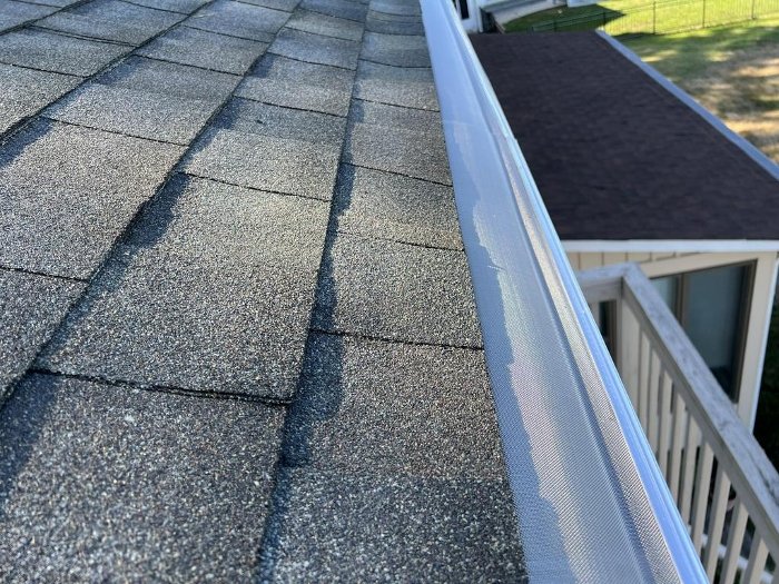 Close-up of a new seamless gutter with micro mesh gutter guards installed along a shingle roof edge.