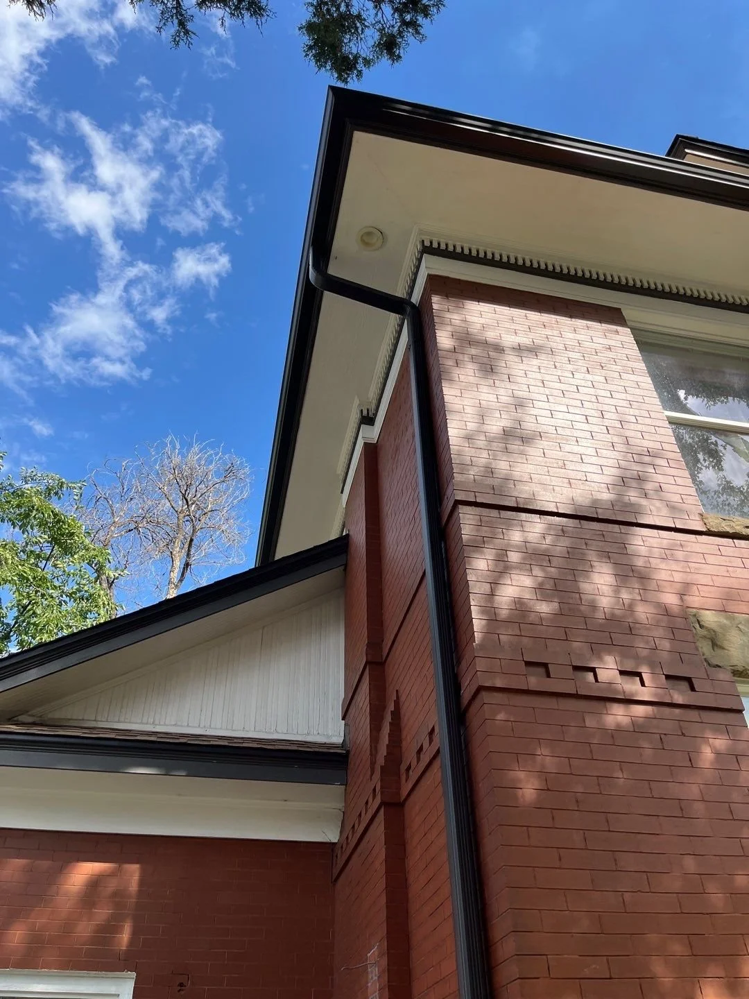 Close-up of a seamless gutter and downspout installed at the corner of a brick home.