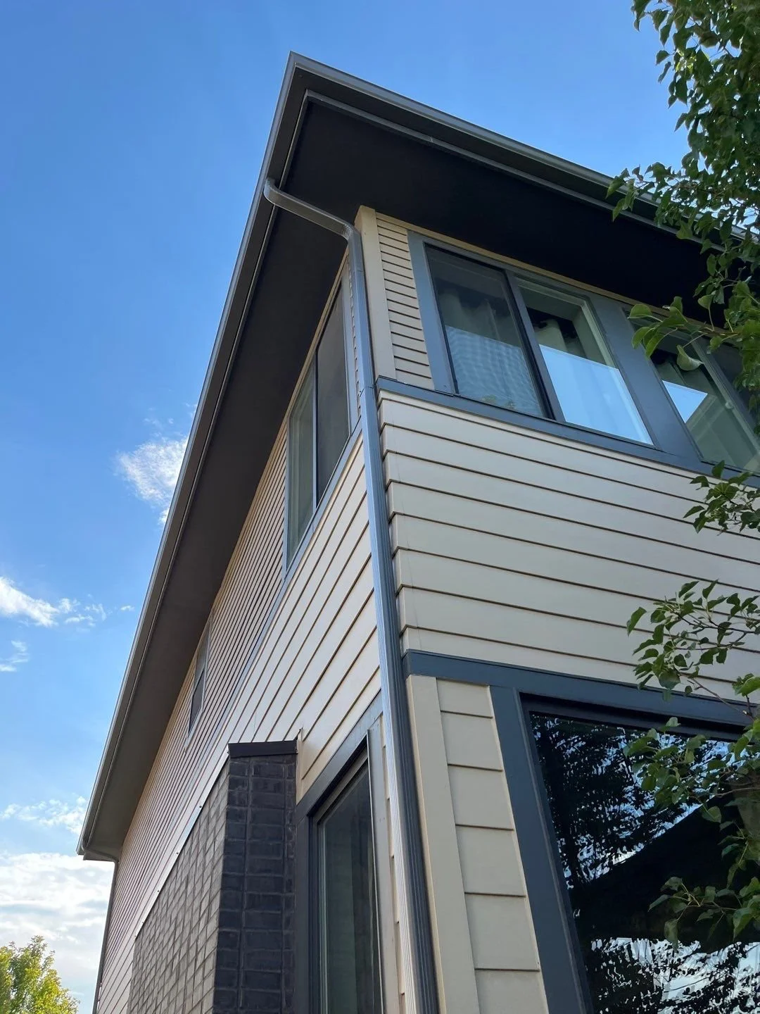 Close-up of a seamless gutter and downspout installed on the upper corner of a two-story home.