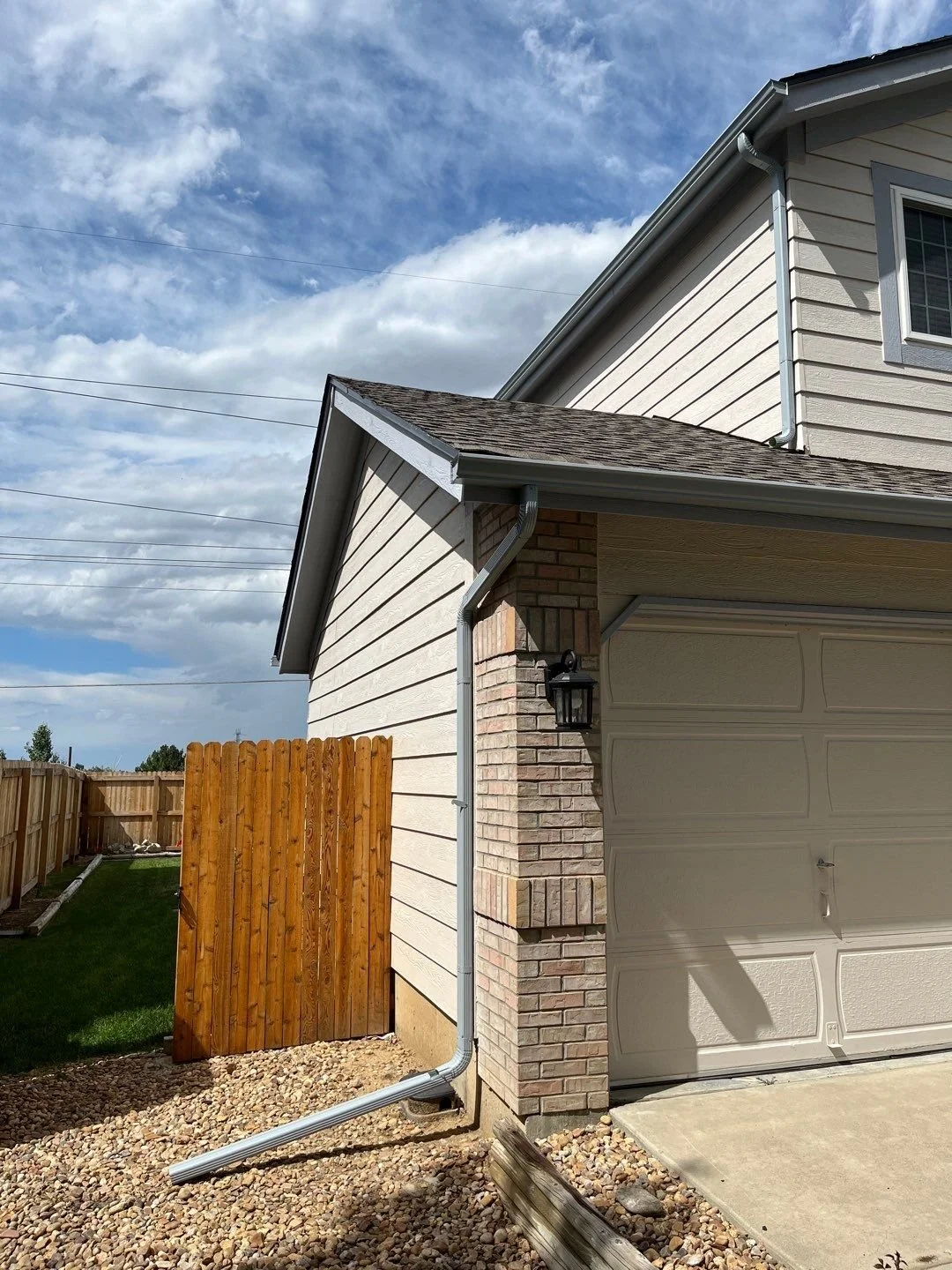 Gray seamless gutter and downspout installed beside the garage of a brick and siding home.