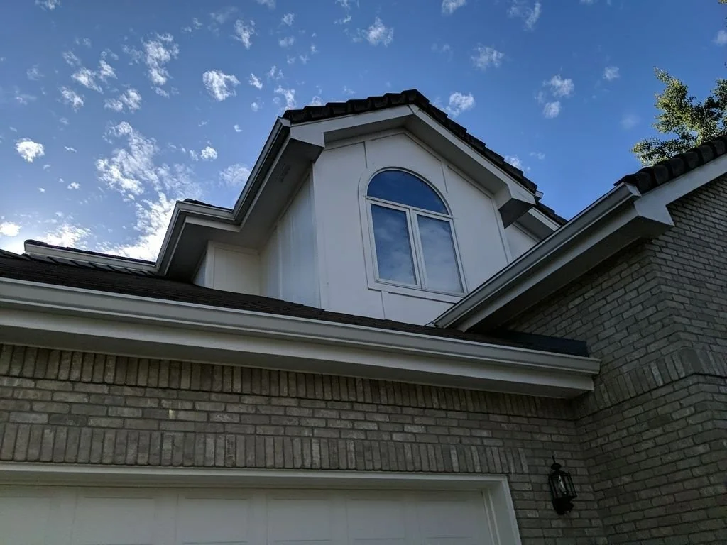 Close-up of a custom seamless gutter installation around an upper dormer and garage roofline.