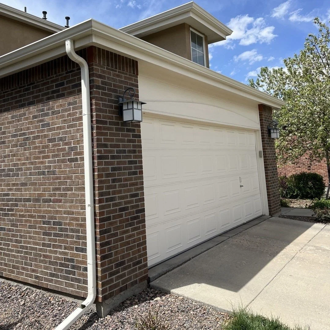 Completed gutter and downspout replacement on a brick and siding garage exterior.