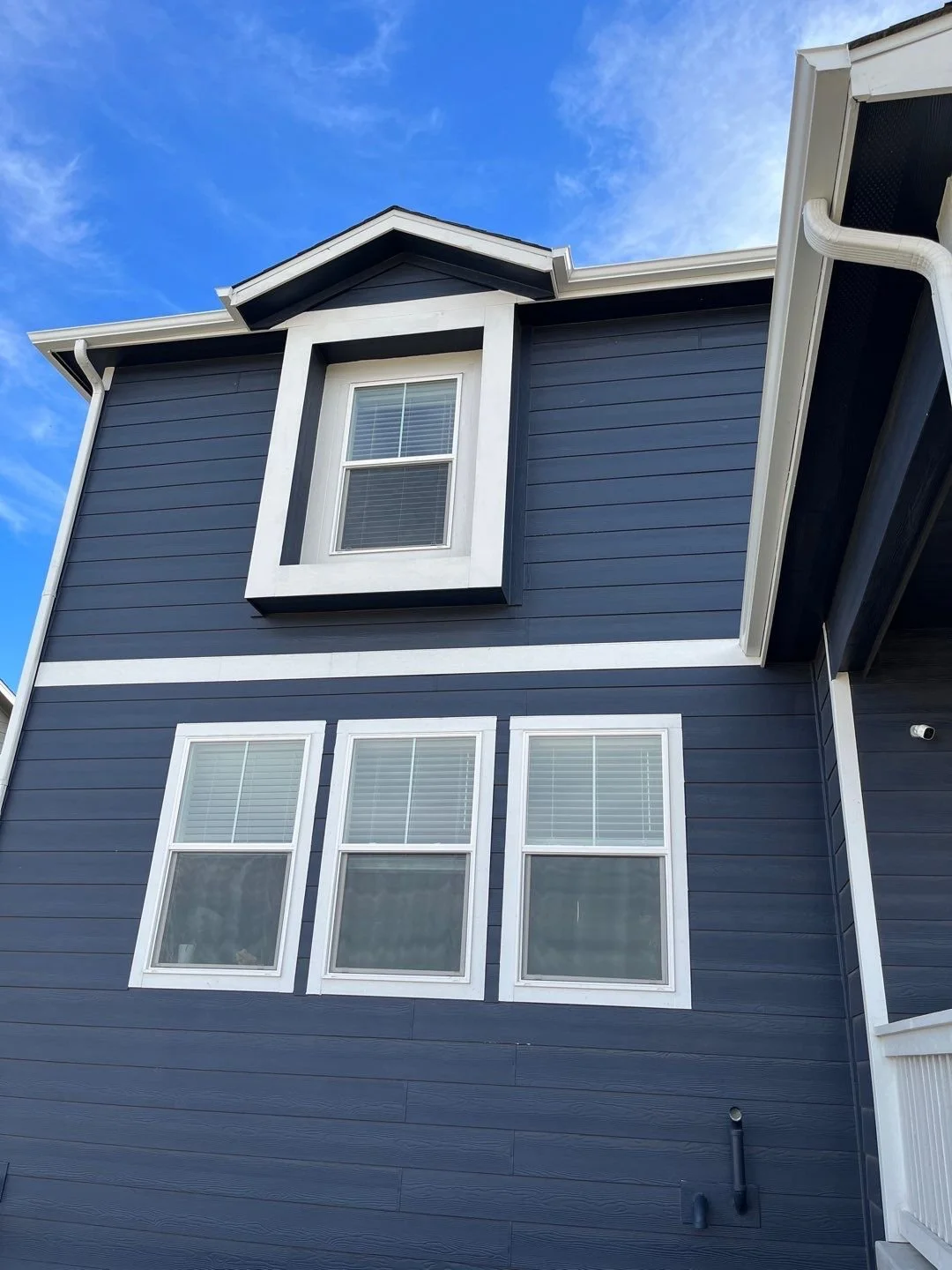 White seamless gutters installed above upper-story windows on a dark blue home.