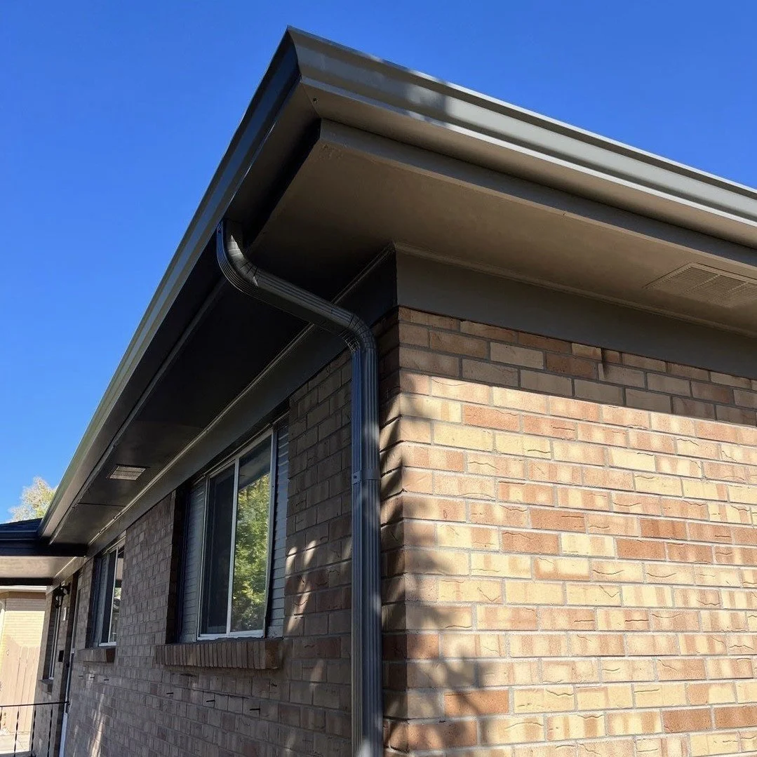 Completed seamless gutter replacement with new gutters and downspouts installed along the roofline of a brick home.