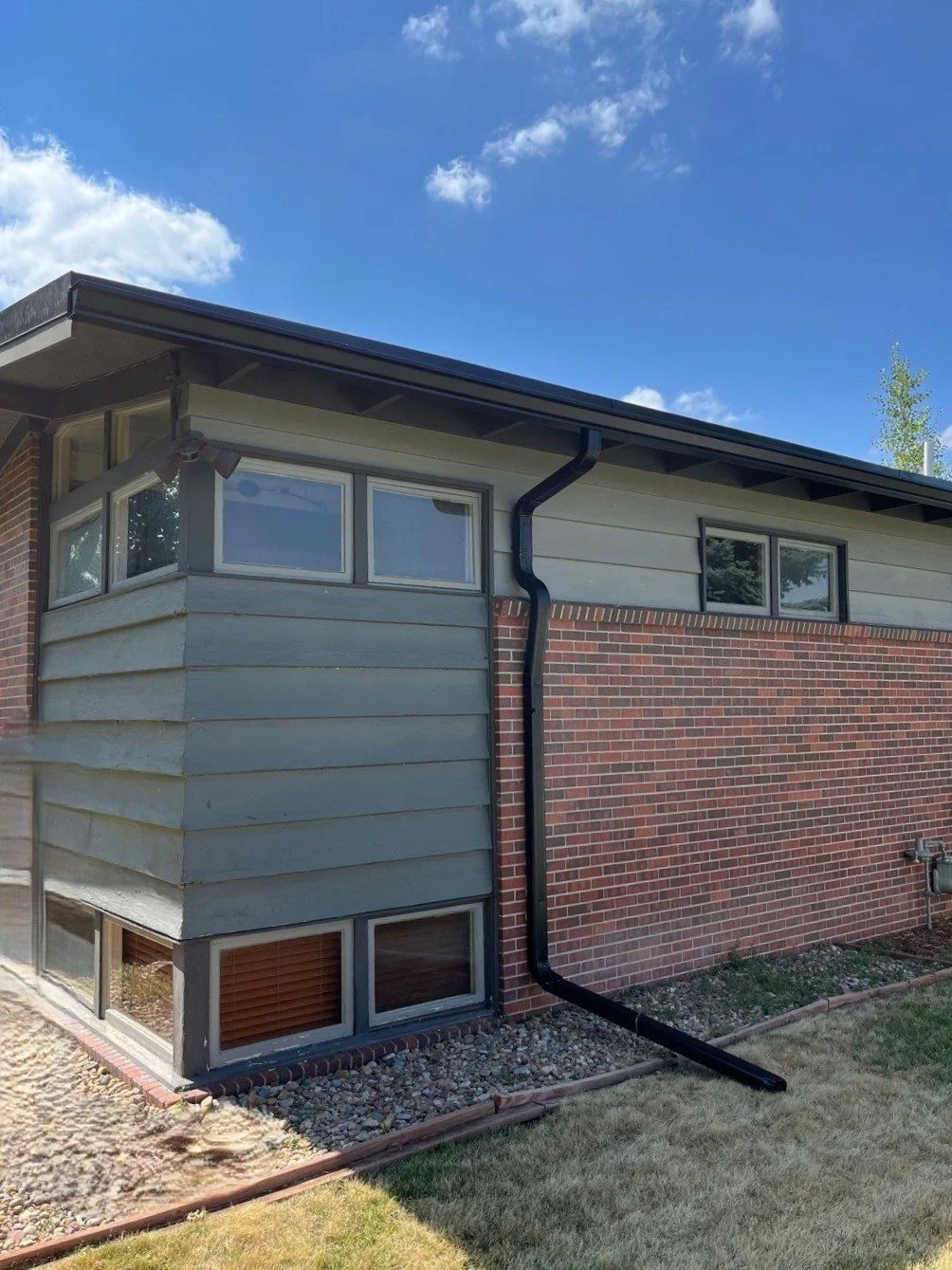 Seamless gutter and downspout replacement completed along the rear corner of a brick-and-siding home.