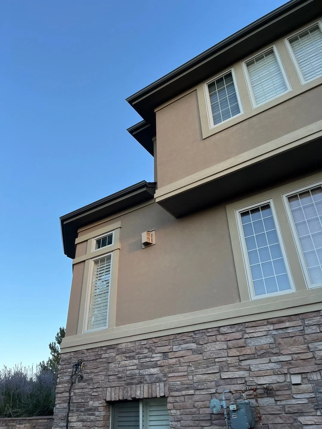 New seamless gutters and downspouts added along the upper corner of a stucco home with stone accents.