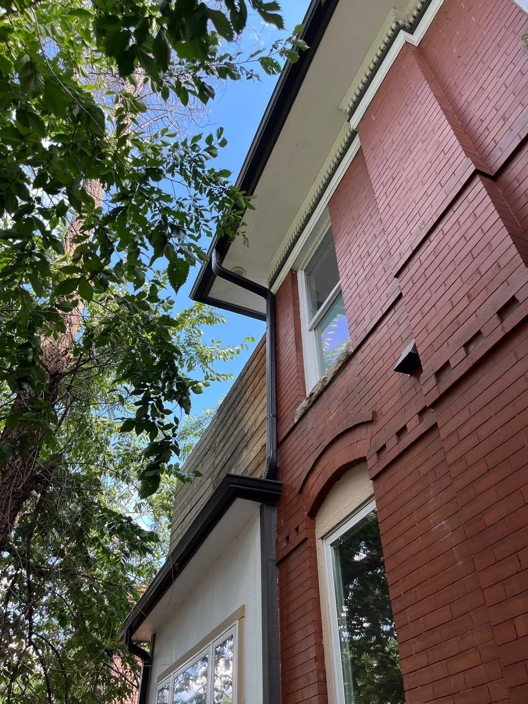 Downspout installed vertically along the exterior wall of a brick home.