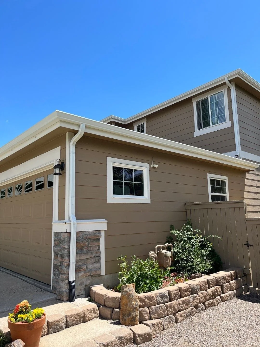 White seamless gutters and downspouts installed along the side of a beige home with stone accents.