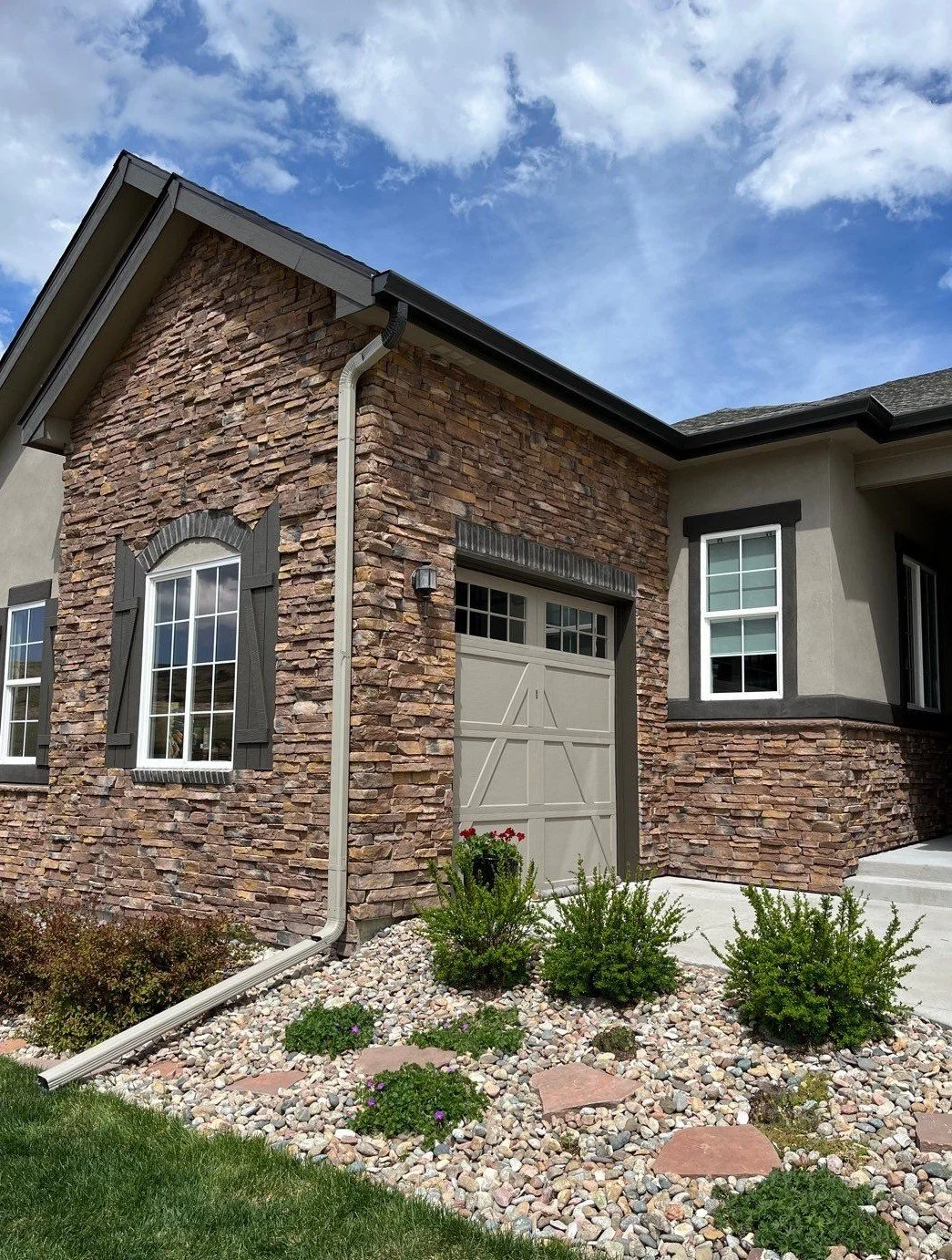 Seamless gutter and downspout installed along the stone garage roofline of a home.
