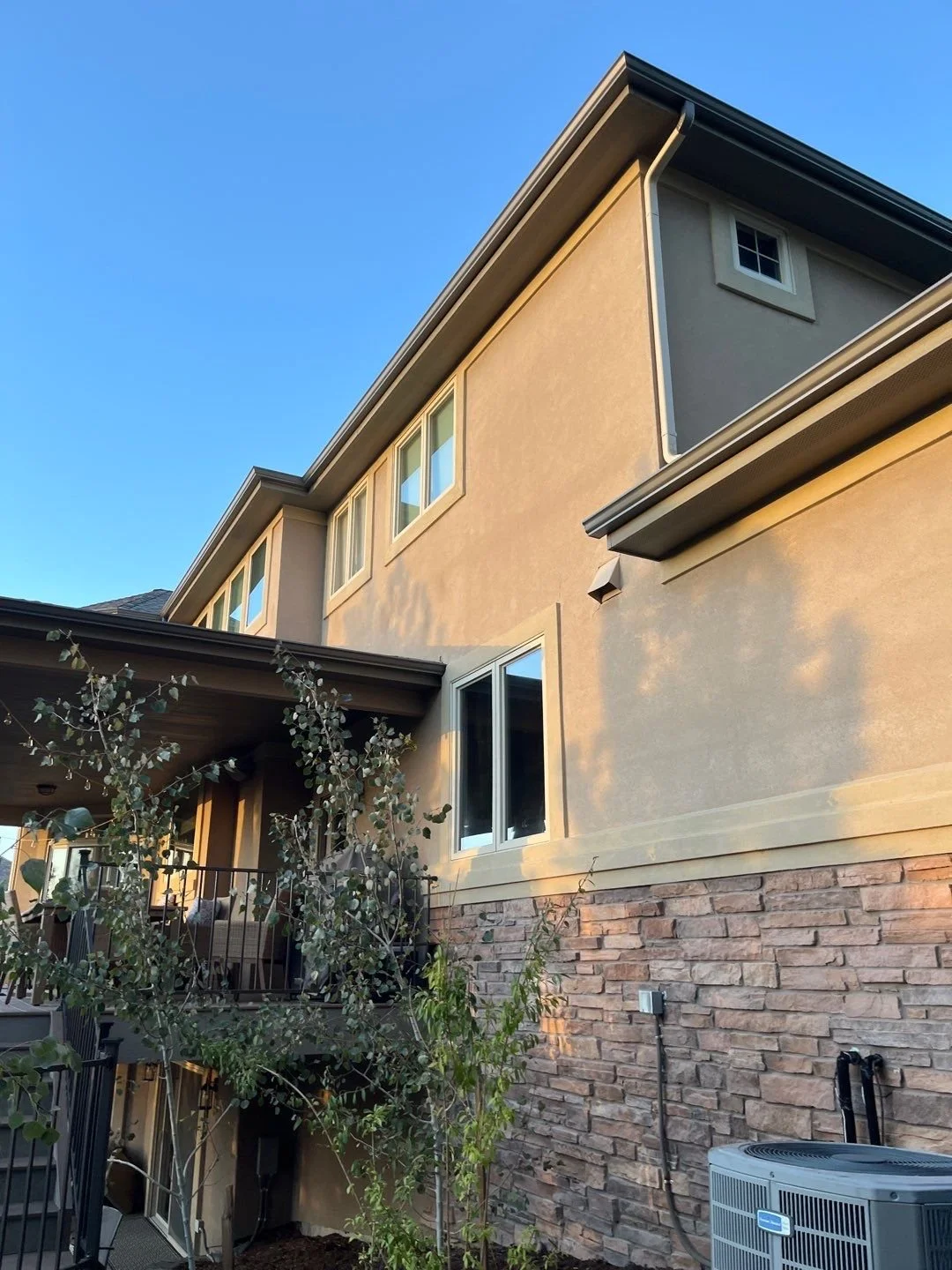 Custom gutters and downspouts fitted to the long side roofline of a stucco and stone residence.