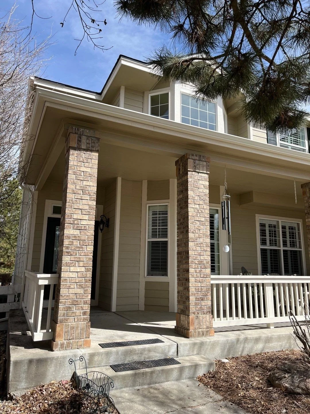Eggshell seamless gutters and downspouts installed around the covered front porch of a tan home.