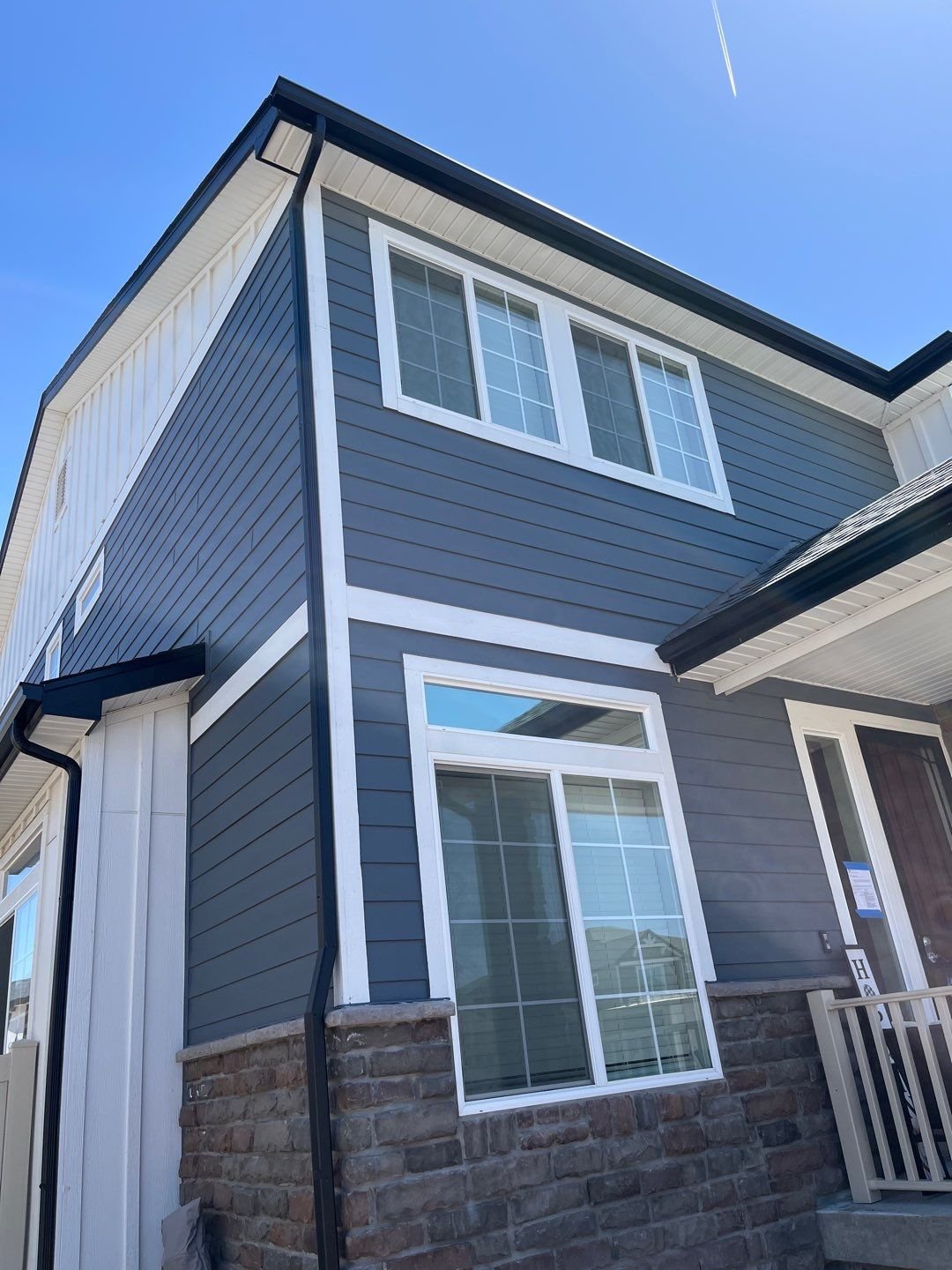 Professional seamless gutter installation on a dark-sided home with multiple upper rooflines.