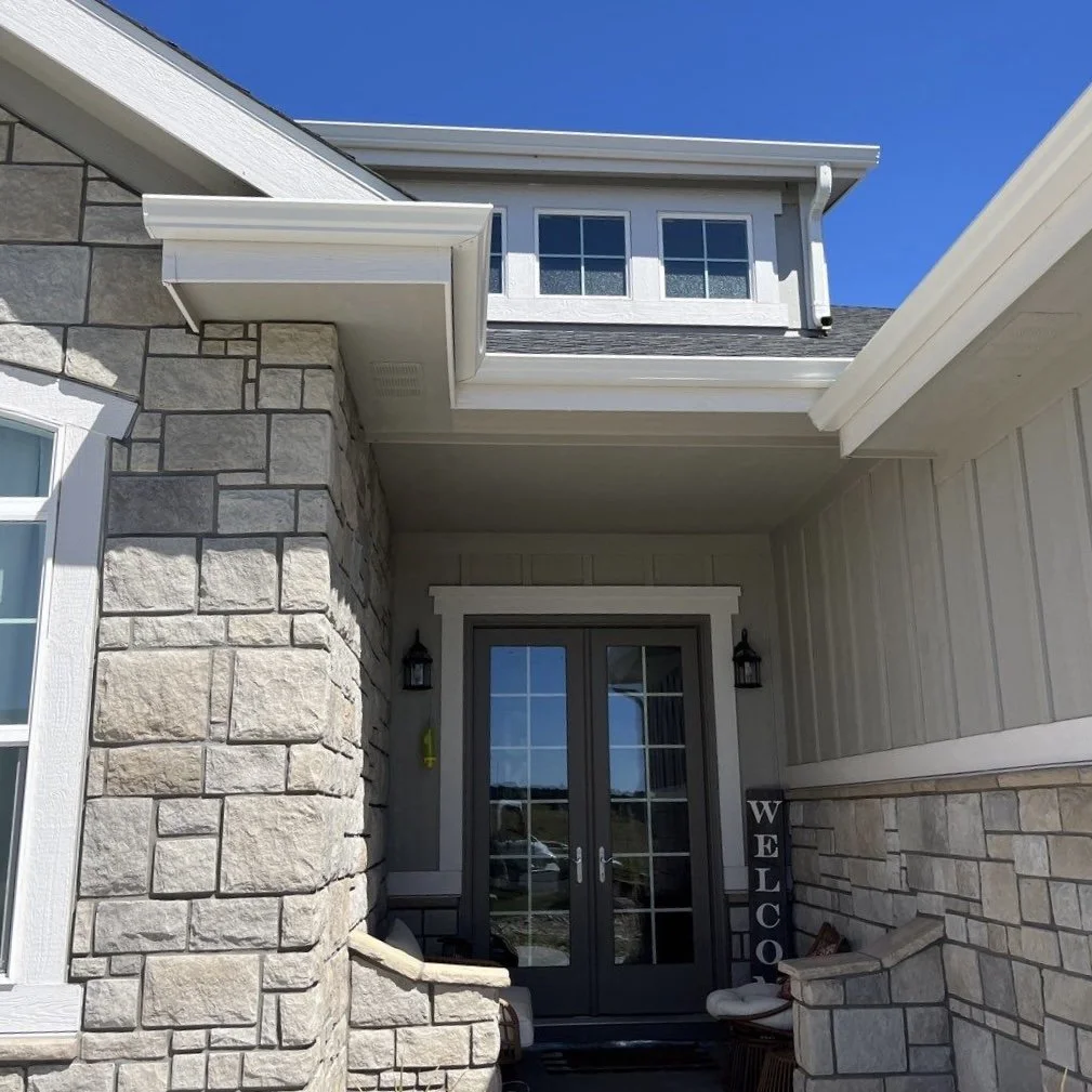 New gutter and downspout system installed above the front entry of a stone-accented home.