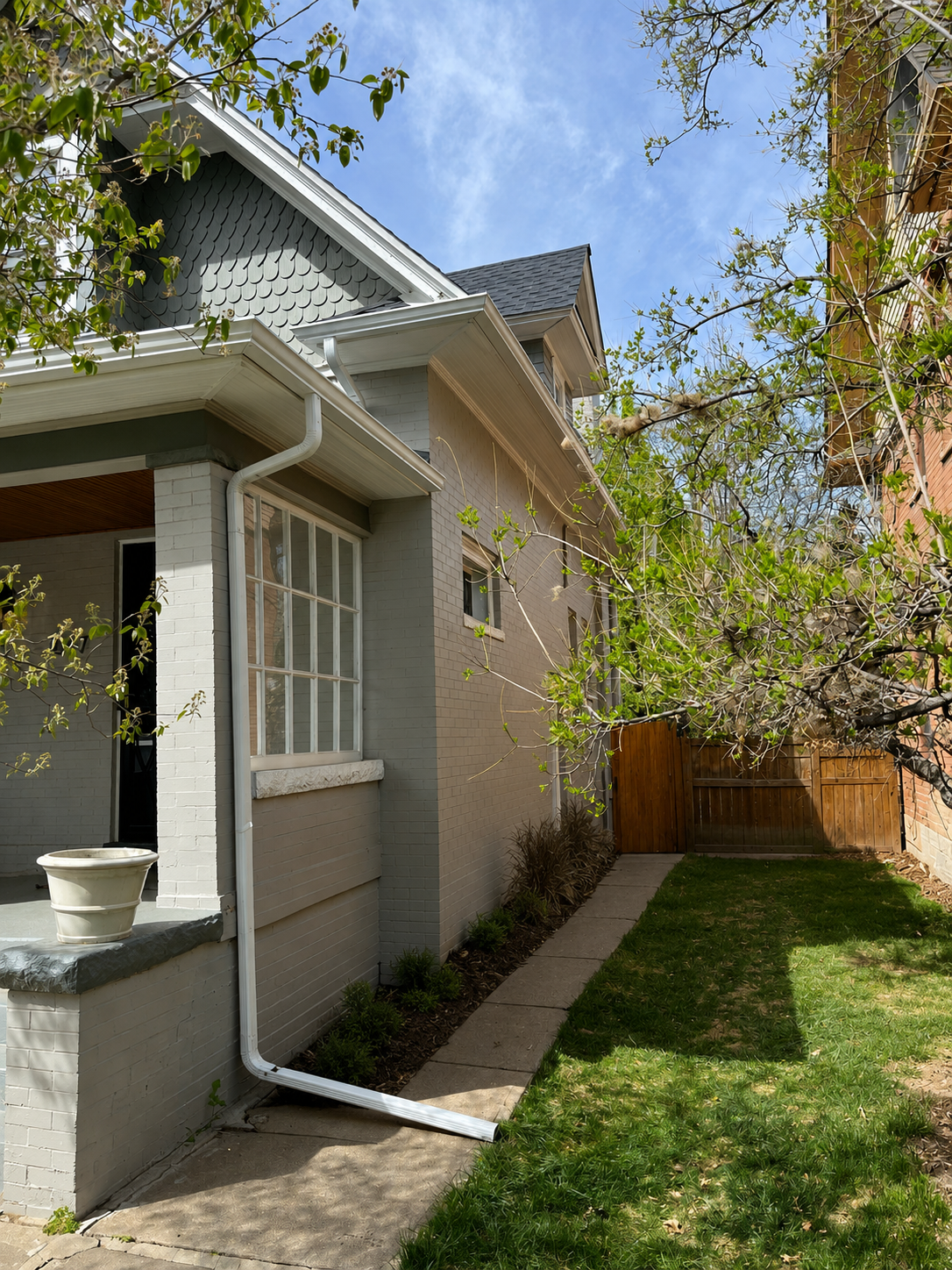 Seamless gutters and downspouts installed along the side of a residential home with a narrow yard.
