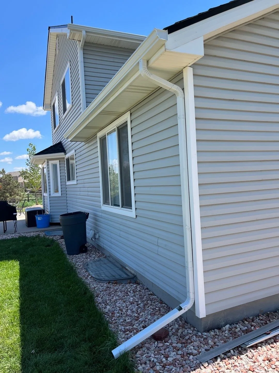White seamless gutter and downspout installed along the side of a blue-sided home.