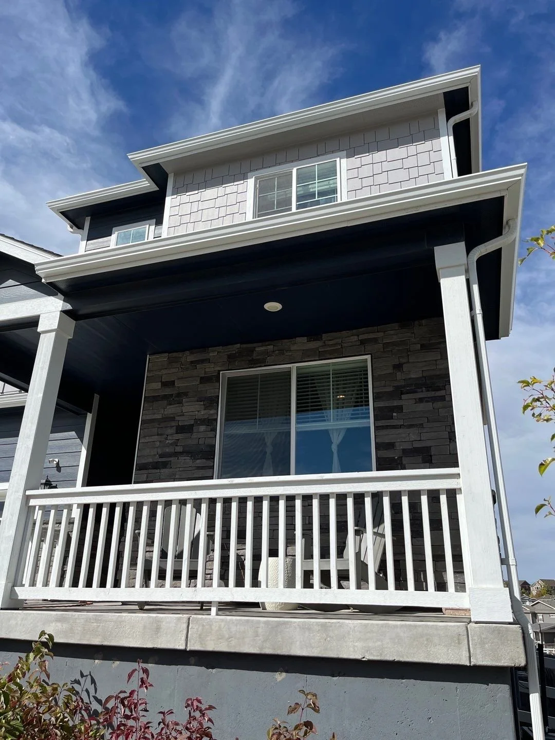 Front porch of a light gray and stone home with white seamless gutters and downspouts.