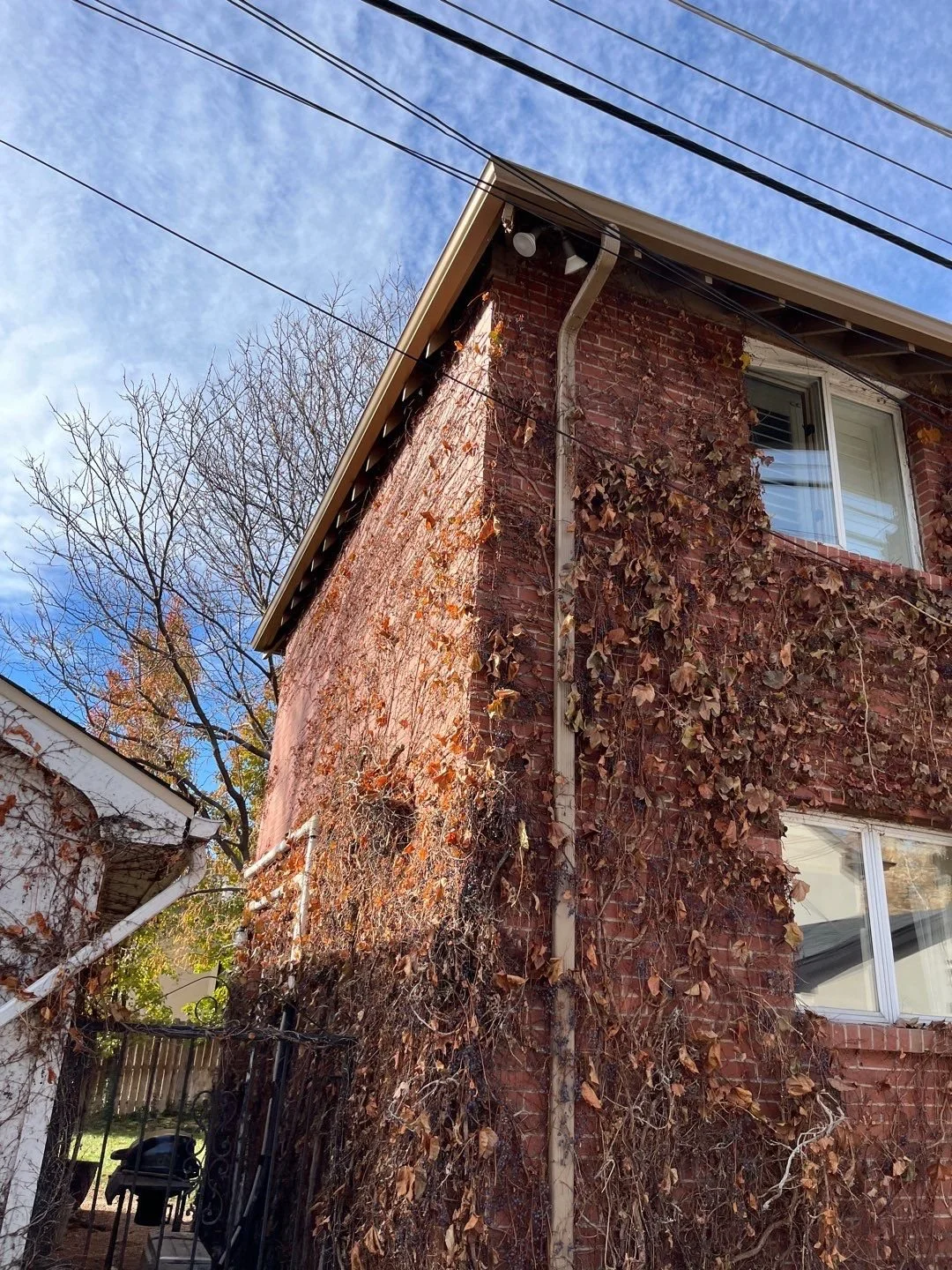 Seamless gutters and downspouts installed along the rear corner of a brick home.