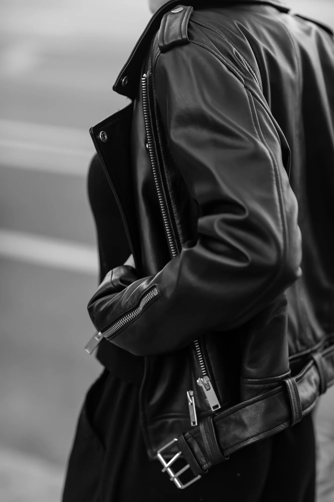 Close-up of a person wearing a black leather jacket with silver zippers, standing outdoors.