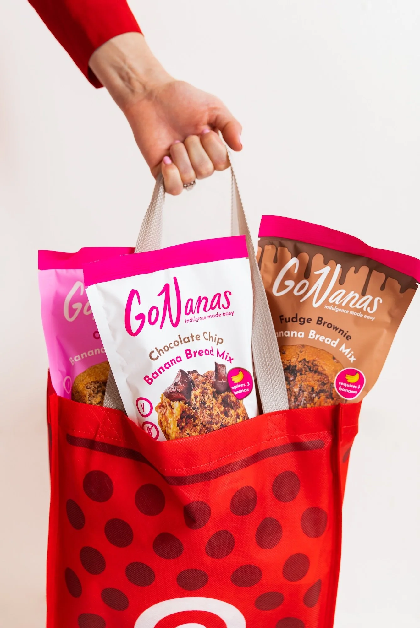 A hand holding a Target shopping bag containing GoNanas banana bread mixes.