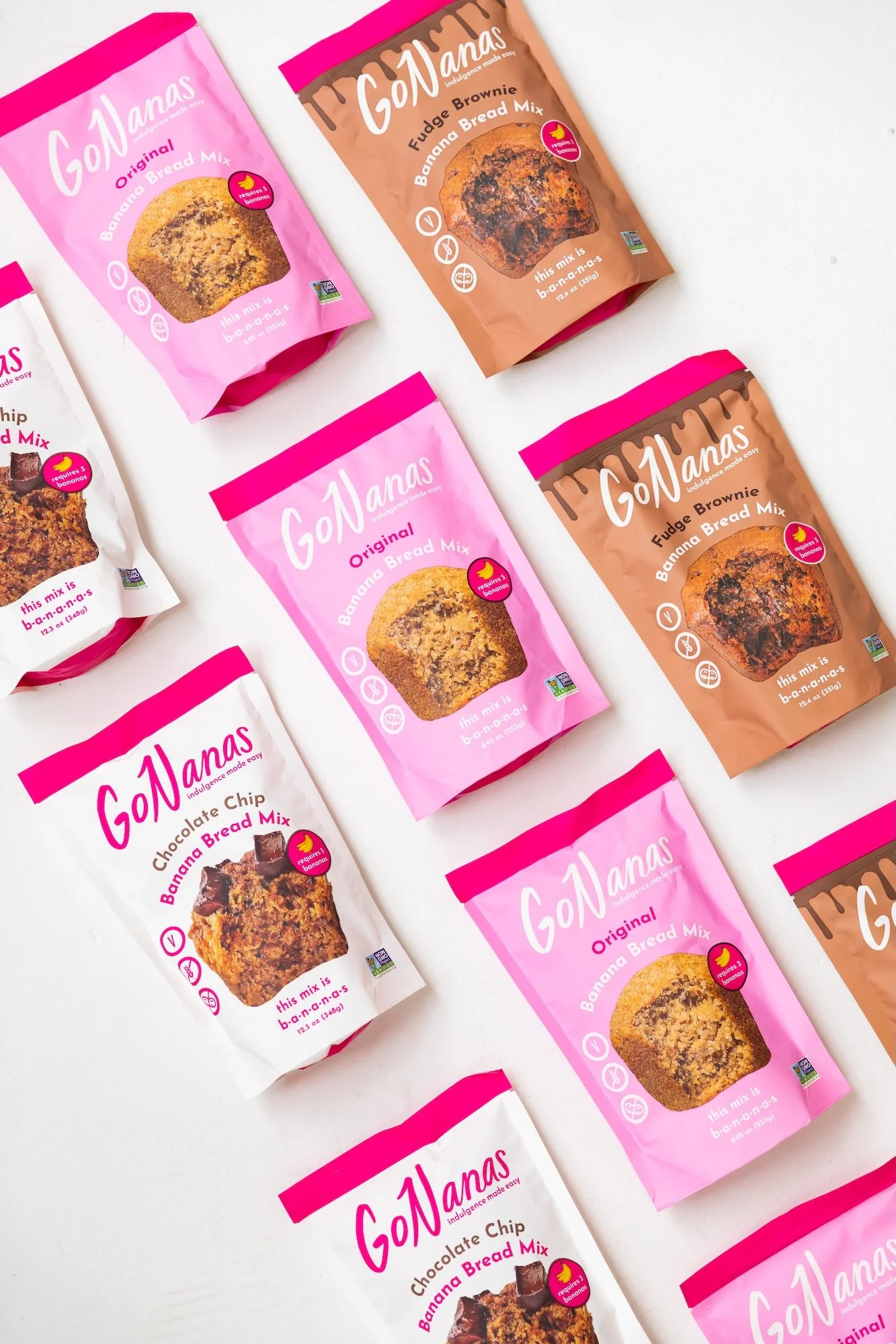 Multiple packages of GoNanas banana bread mix, including original, fudge brownie, and chocolate chip flavors, arranged on a white surface.