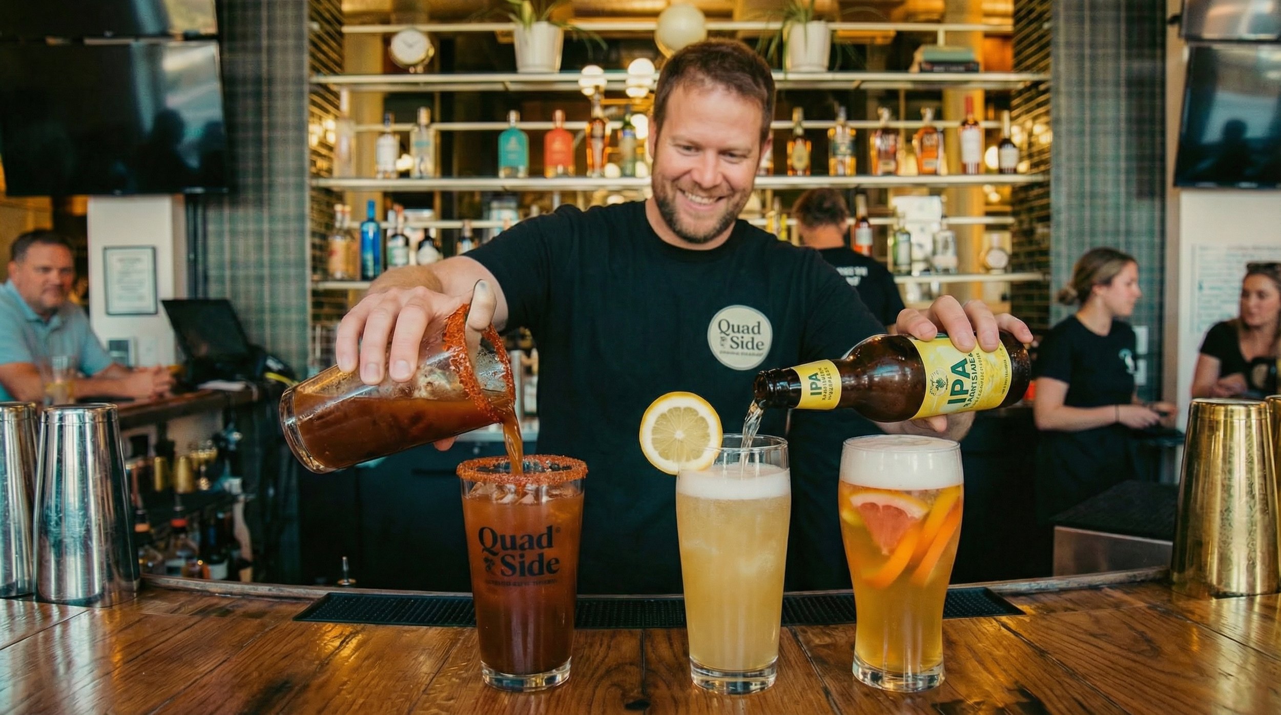 Bartender at a bar pouring drinks into three glasses with lemon slices, with a background of shelves filled with bottles and patrons sitting at the bar.