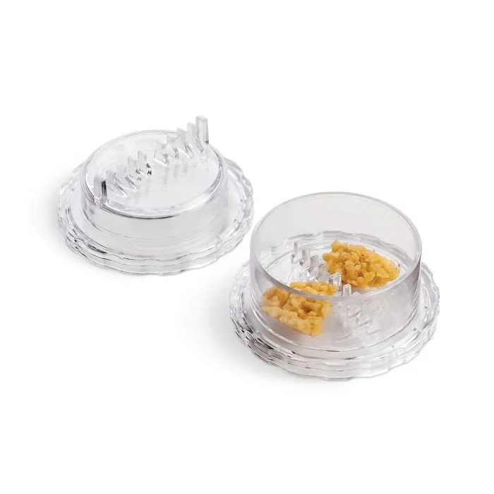 A clear plastic garlic twist mincer containing two garlic cloves.
