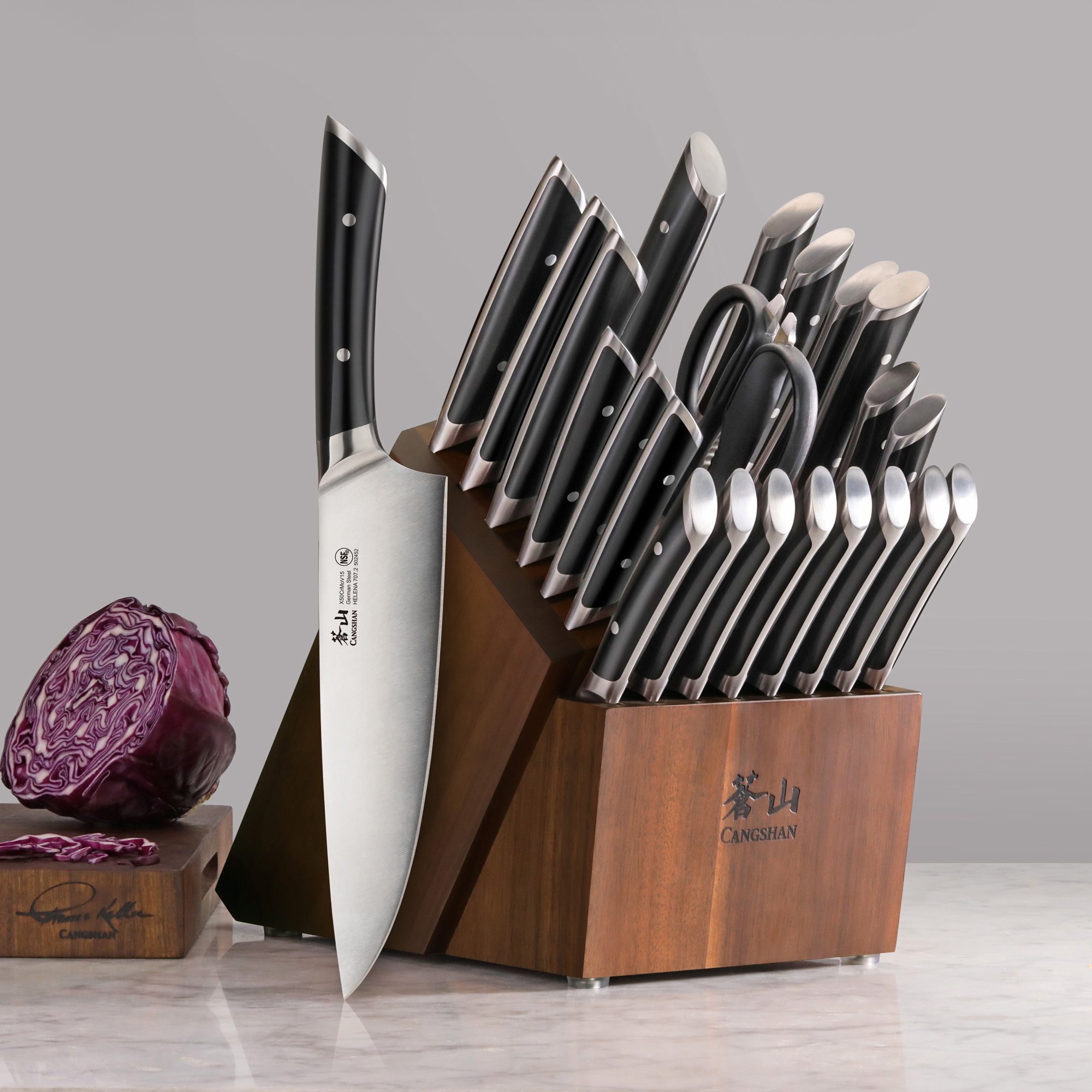 Set of Cangshan kitchen knives and scissors stored in a wooden knife block on a marble countertop, with a halved purple cabbage on a small cutting board next to it.