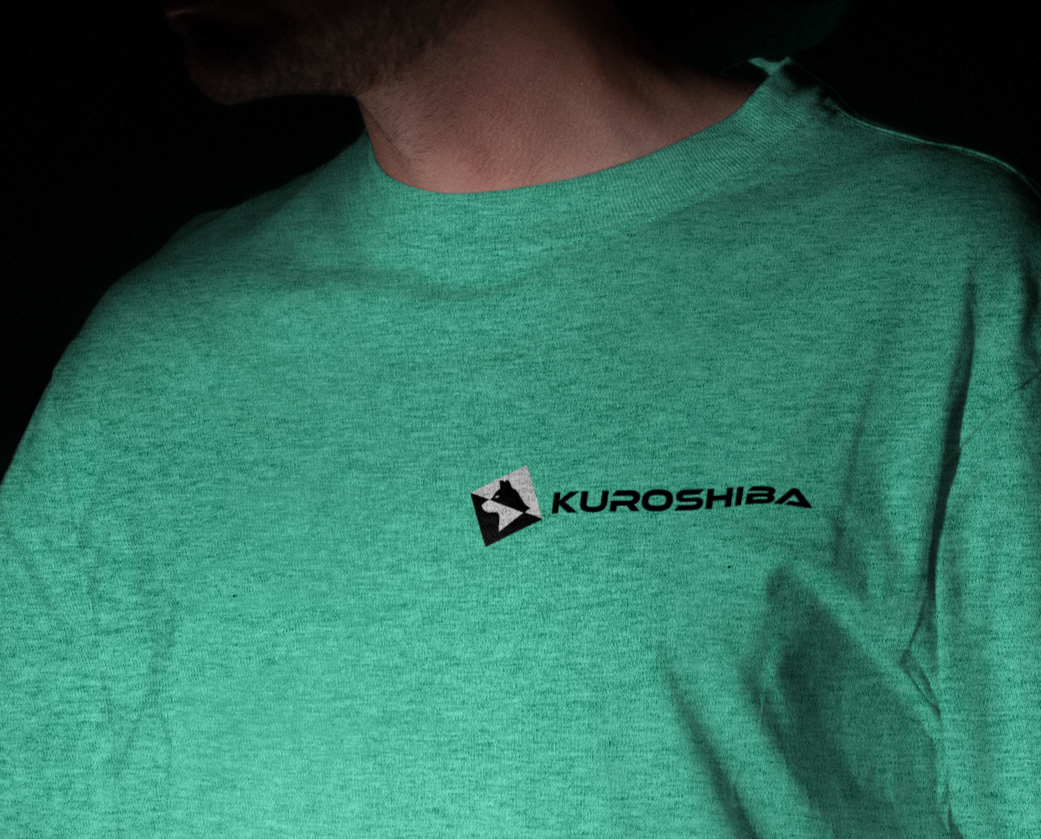 Close-up of a person wearing a teal T-shirt with a Kuroshiba logo on the chest.