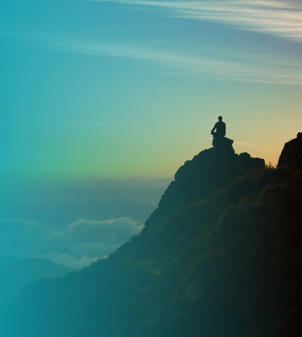 A person sits atop a rocky mountain, looking out at a beautiful sunrise