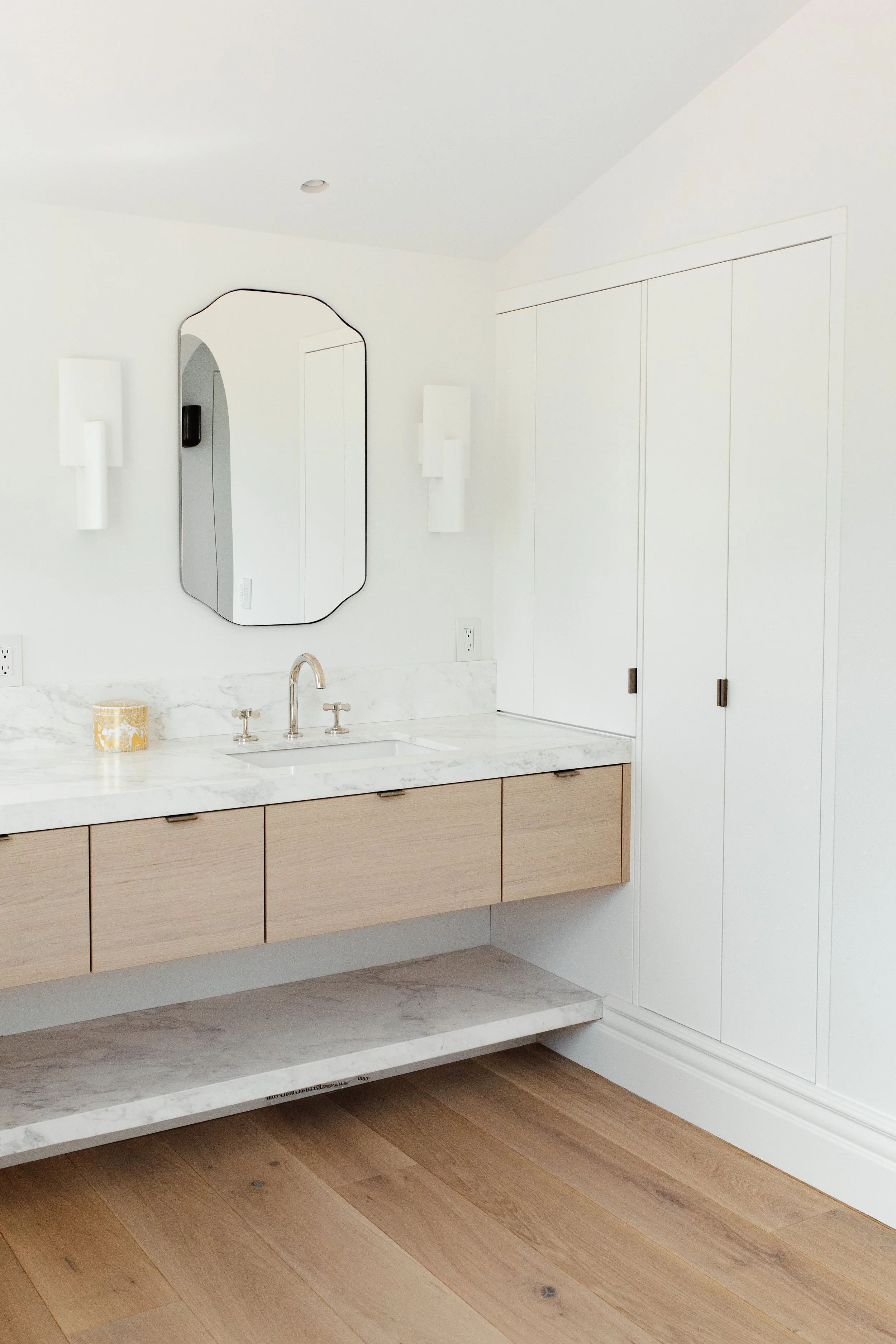 Modern, coastal, floating bathroom vanity and custom built-in medicine cabinet. Vanity is made from white oak material with modern slab drawer fronts, marble countertop and lower shelf, and nickel fixtures. Medicine cabinet is painted white.
