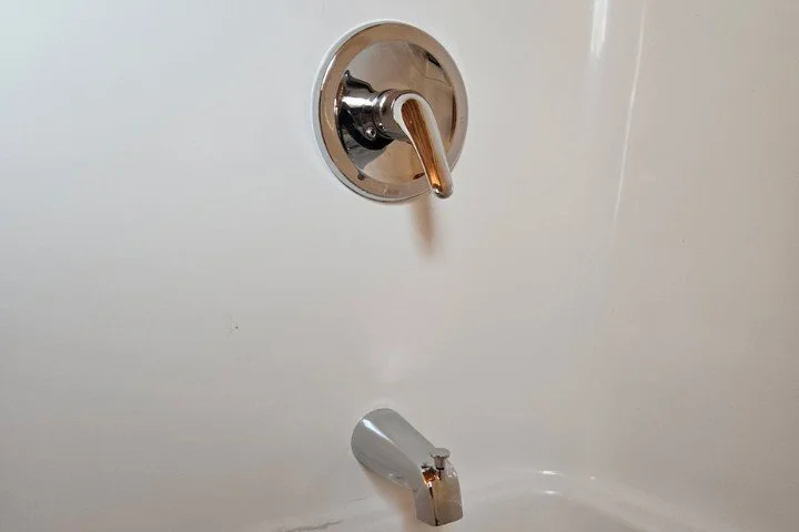 Close-up of a bathtub faucet and water control lever on a white wall.