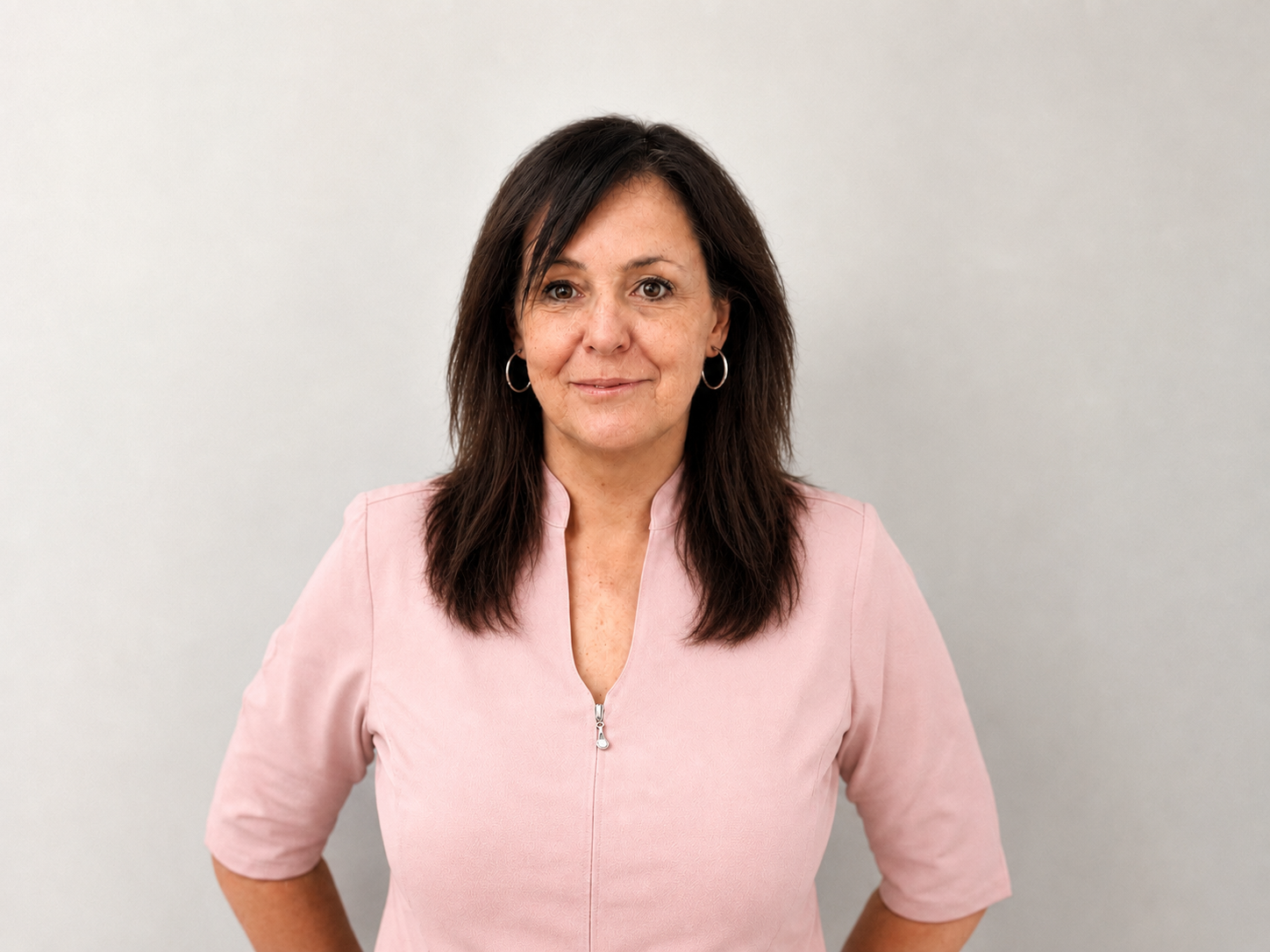 Portrait of a woman with dark hair, wearing a black jacket, standing against a plain white wall.