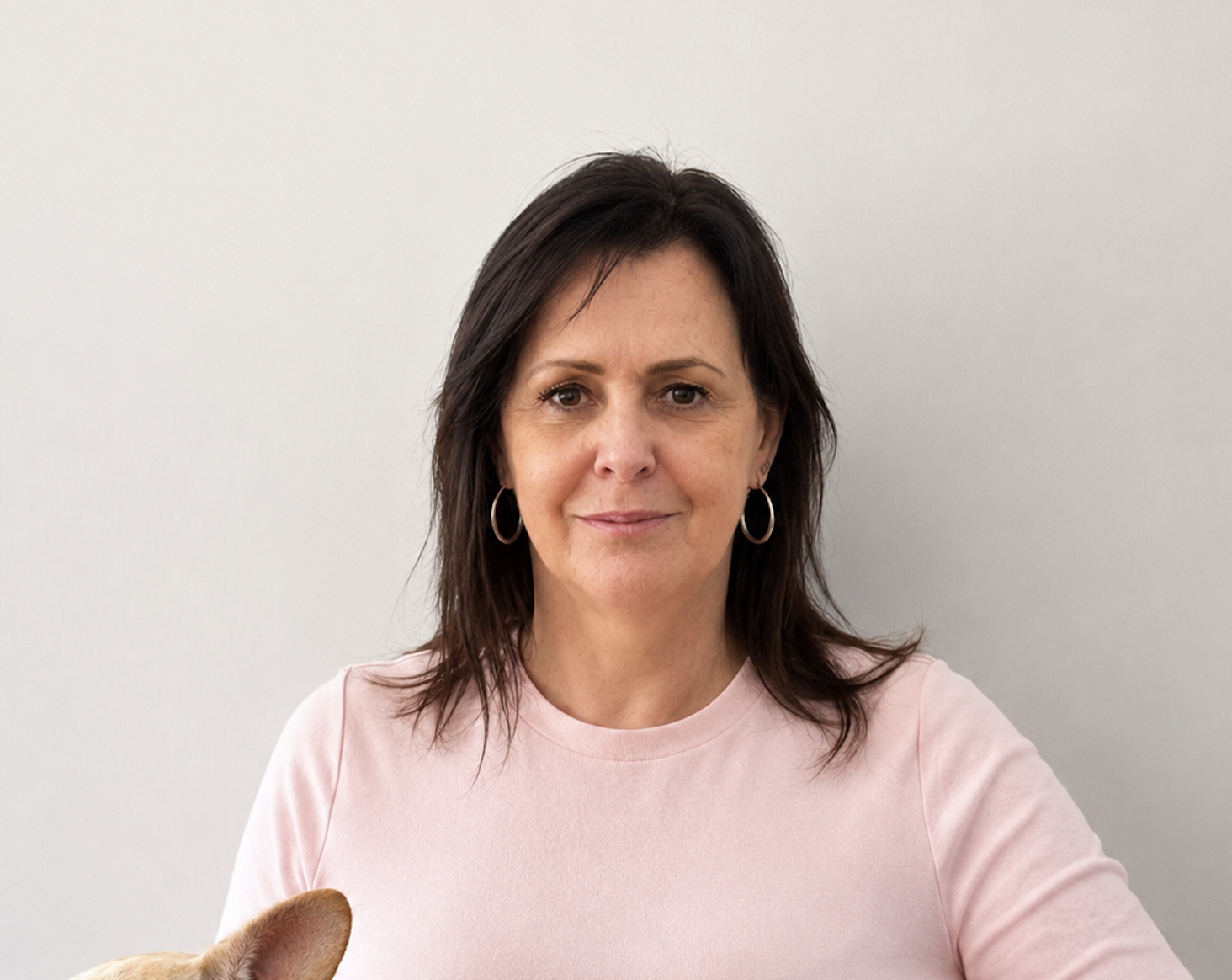 Portrait of a woman with dark hair, wearing a black jacket, standing against a plain white wall.