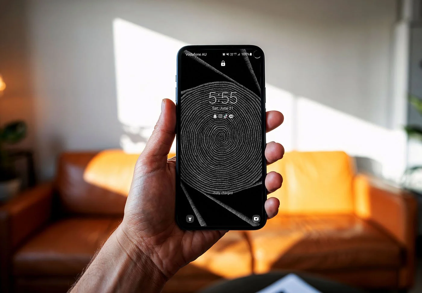 Person-holding-phone-with-black-and-white-line-art-and-lockscreen-over-living-room-background-with-orange-leather-couch