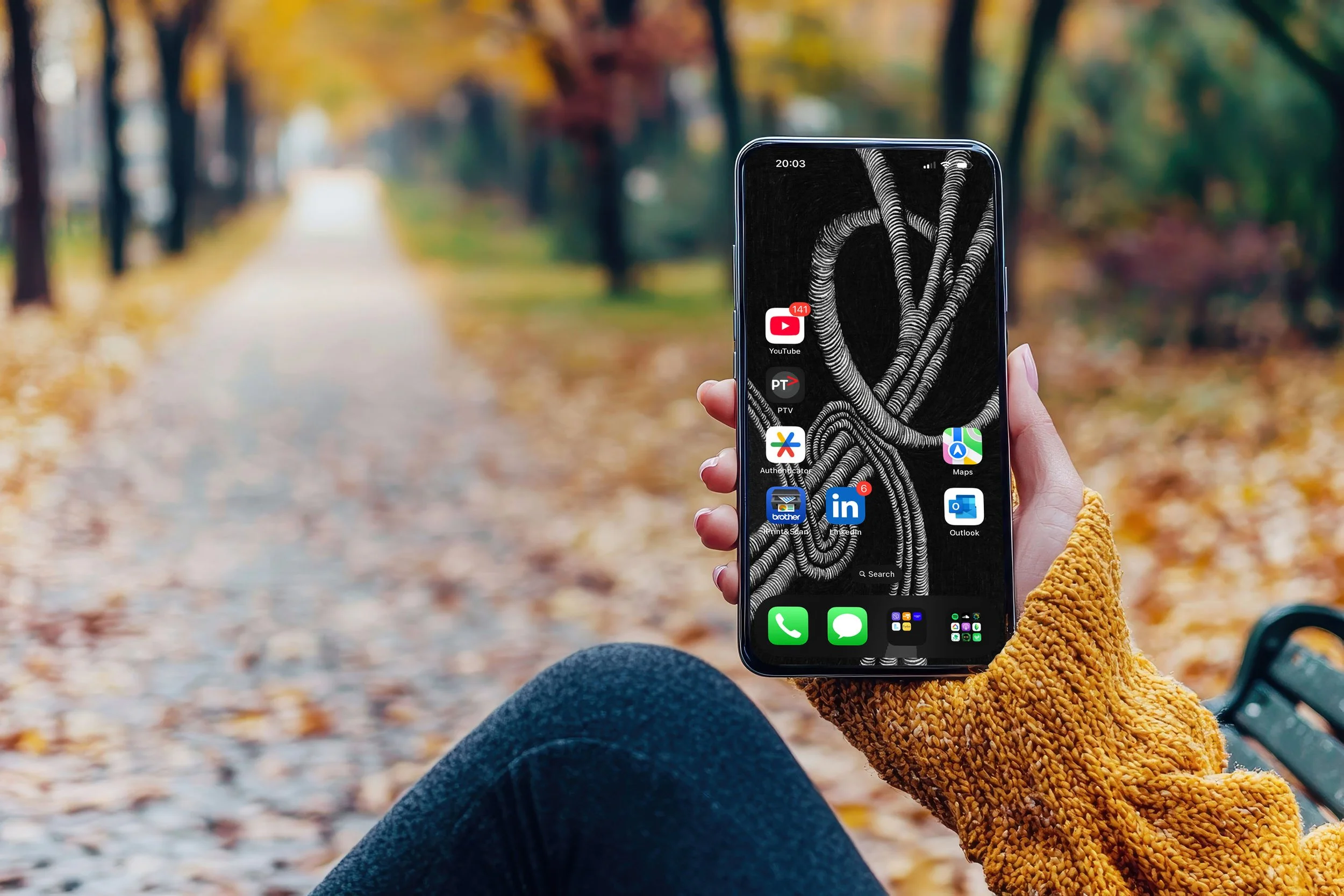 Women-wearing-yellow-sweater-and-dark-blue-jeans-sitting-on-park-bench-with-trees-and-autum-leaves-holding-iphone-displaying-unsonscious-flow-line-art-and-app-icons.jpg