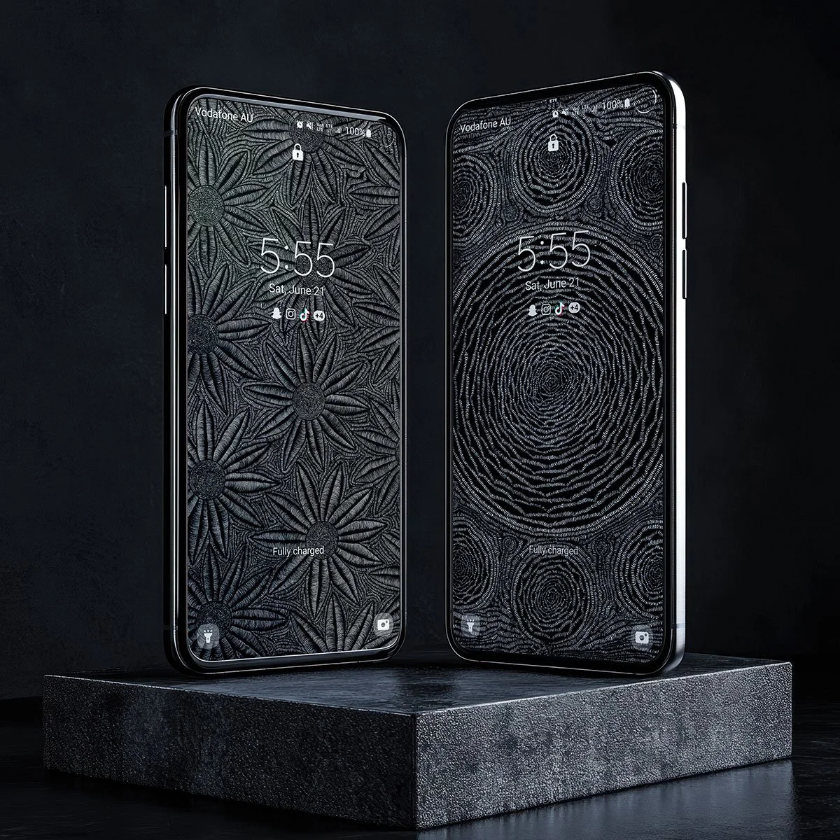Two smartphones with black and white patterned screens, set on a textured black platform against a black background.