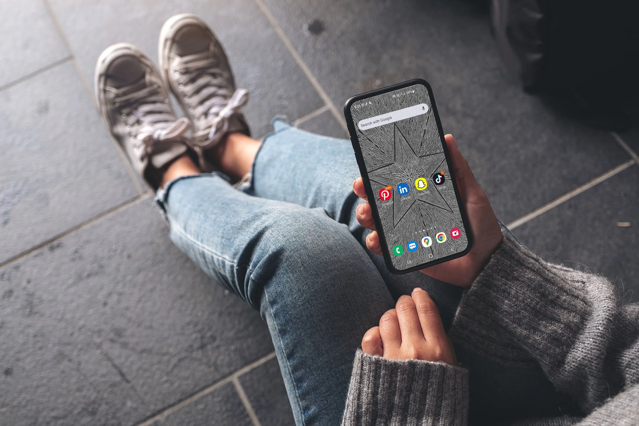 Girl-wearing-jeans-and-woolen-sweater-sitting-holding-samsiung-phone -ith-black-and-white-line-art-wallpaper-with-app-icons.jpg