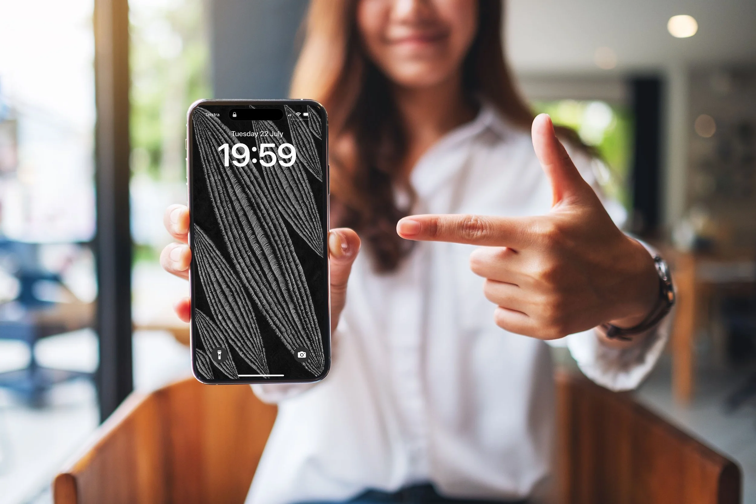 Women-standing-in-cafe-with-blurred-background-holding-and-pointing-to-an-apple-phone-with-lockscreen-of-unsonscious-flow-line-art.jpg
