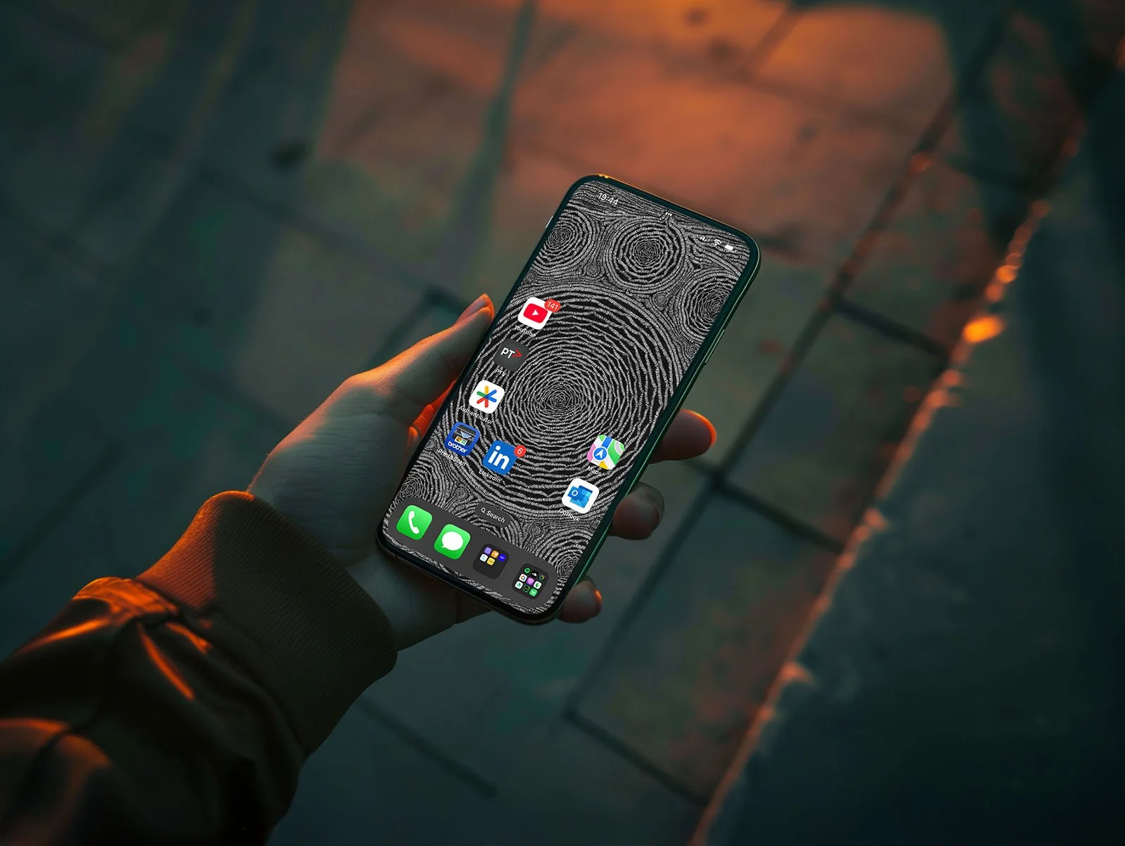 Person-holding-Iphone-with black-and-white line-art-wallpaper-with-homscreen-and-app-icons-over-pavment-at-night.jpg