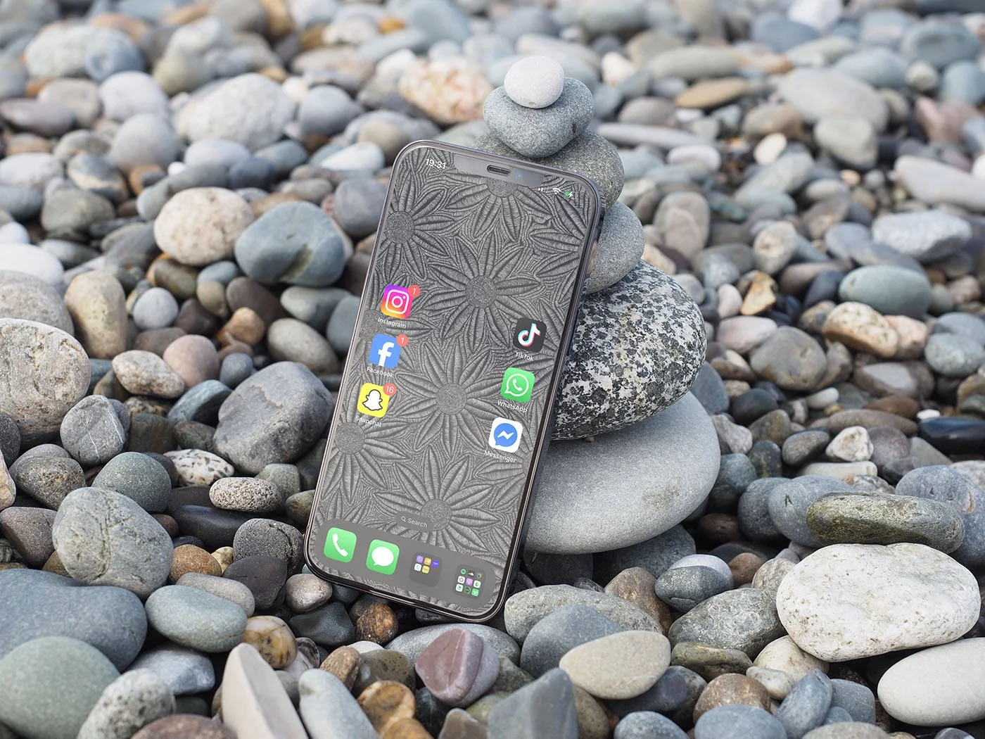 Iphone-with-black-and-white-line-art-wallpaper-and-app-icons-leaning-against-grey-blue-and-white-beach-pebbles