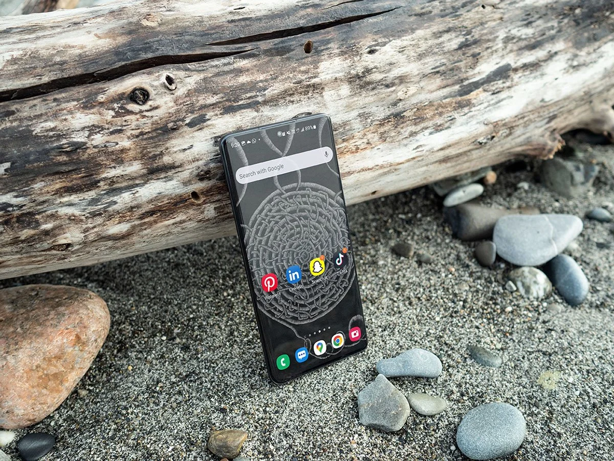 Samsung-phone-with black-and-white line-art-wallpaper-with-homescreen-and-app-icons-standing-slanted on-drift-wood-at-the-beach.jpg
